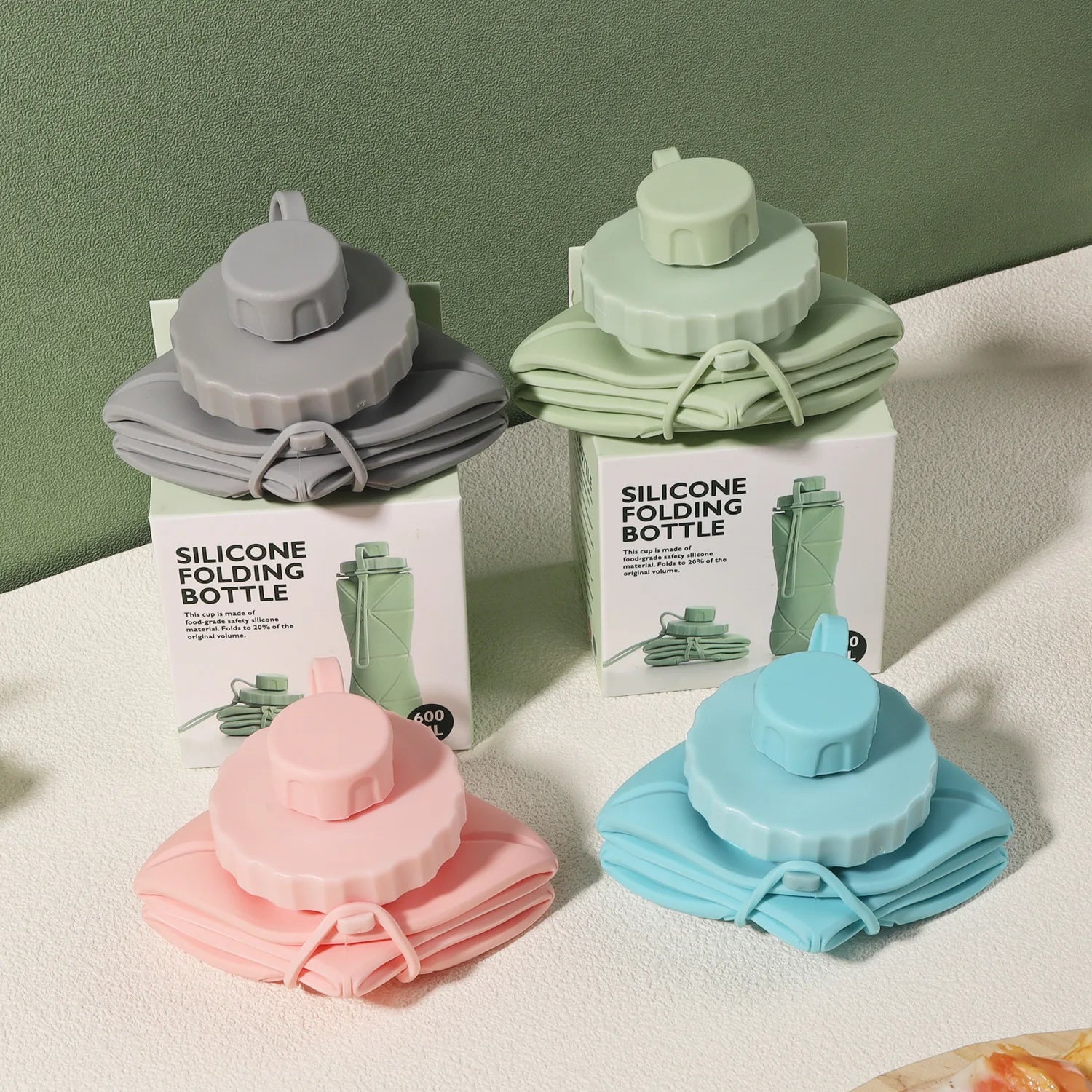 Bouteilles Flexi Hydra pliées en silicone, présentées en quatre couleurs : rose, bleu, vert et gris, avec leur boîte d’emballage.