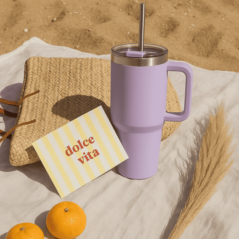 Travel Cup lavande HydraLunch posée sur une serviette de plage, avec carte "dolce vita" et décor estival.